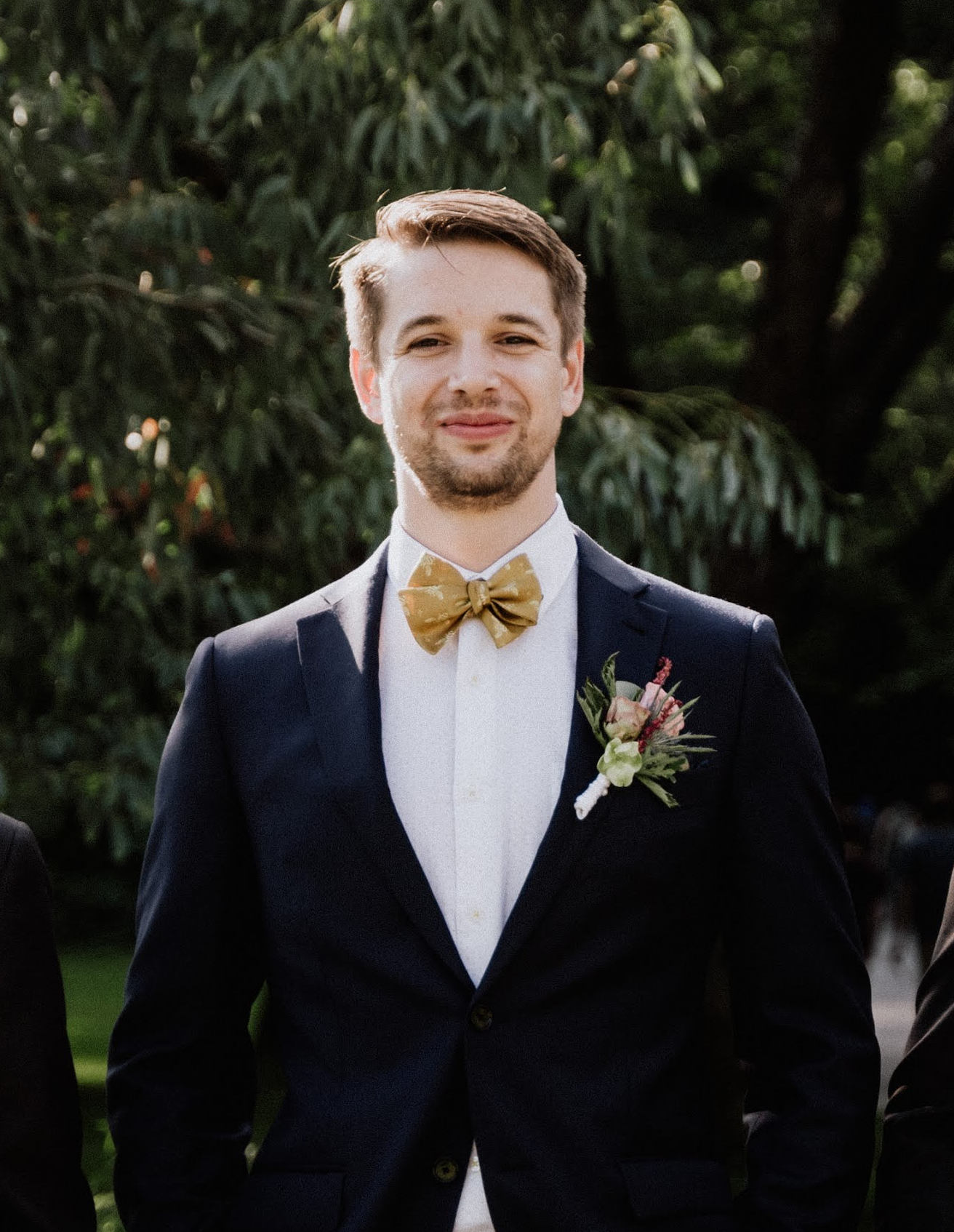 Maks Fisli smiling in a dark suit with flowers and a bow tie